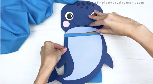 hands gluing body to paper bag whale craft