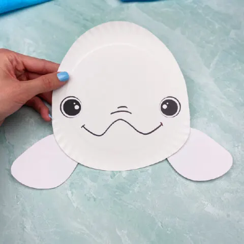 hand holding paper plate beluga whale craft