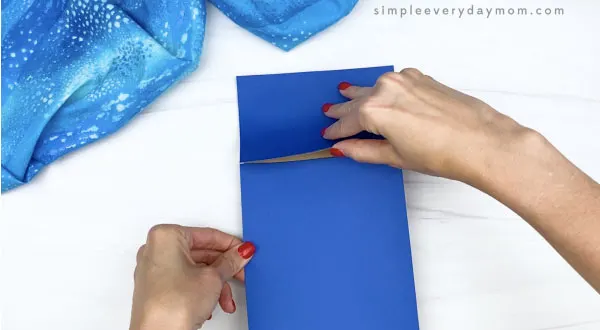 hand gluing blue paper to brown paper bag