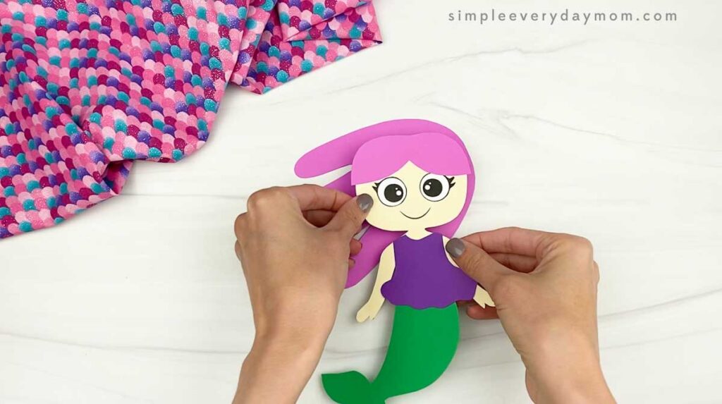 Hands attach the final hair piece to complete a paper mermaid craft.