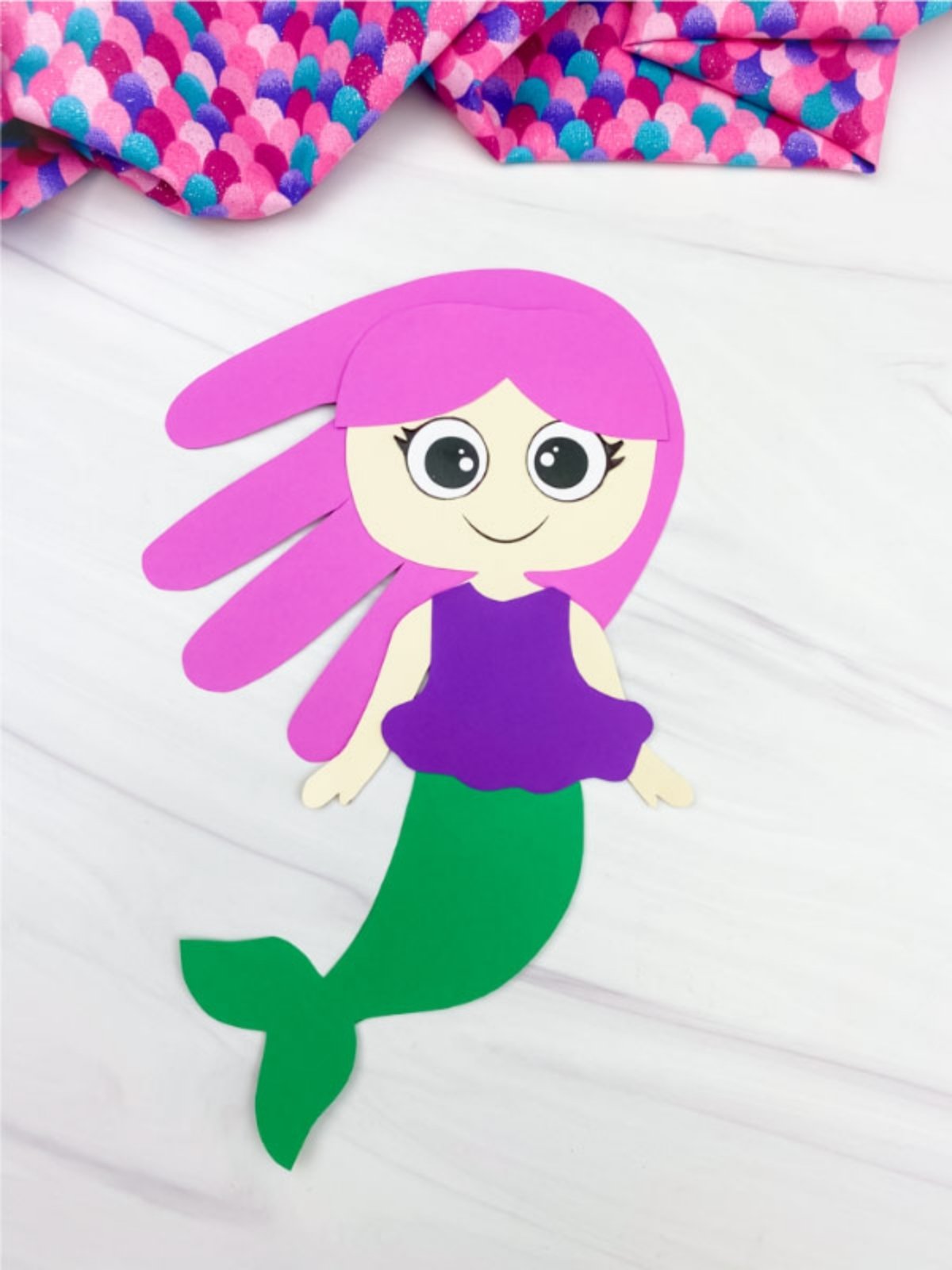 Single paper mermaid craft with pink hair and a green tail on a white background.