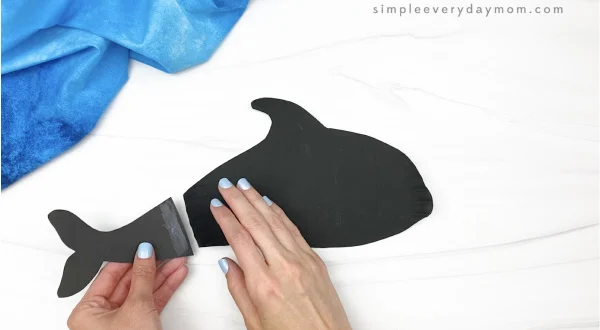hand gluing tail fluke to paper plate whale
