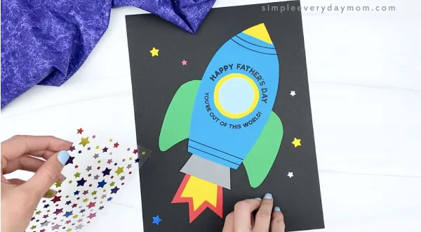 hand placing star stickers on rocket father's day card