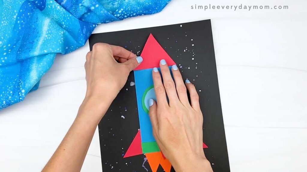 Hands attaching a red triangular nose cone to the top of the rocket.