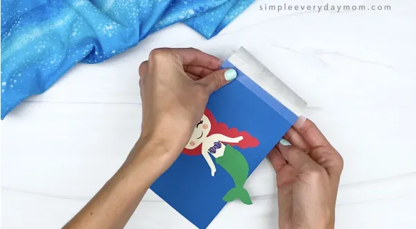 hand taping mermaid template onto toilet paper roll