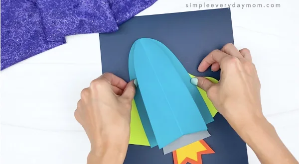 hand gluing 3d rocket onto dark blue paper