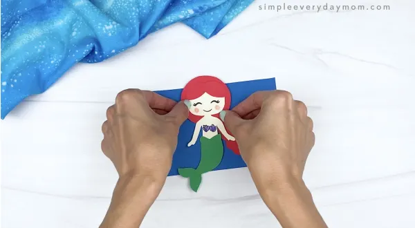 hand gluing mermaid to blue rectangle