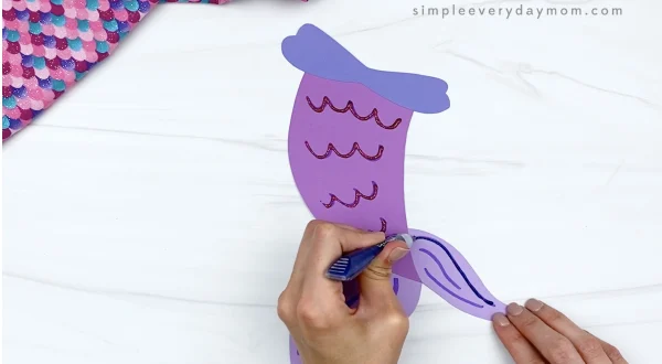hand using glitter glue on mermaid tail craft
