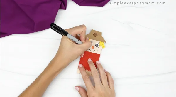 hand drawing smile onto popsicle stick scarecrow craft