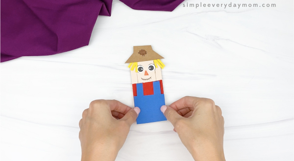 hand gluing overalls onto popsicle stick scarecrow craft