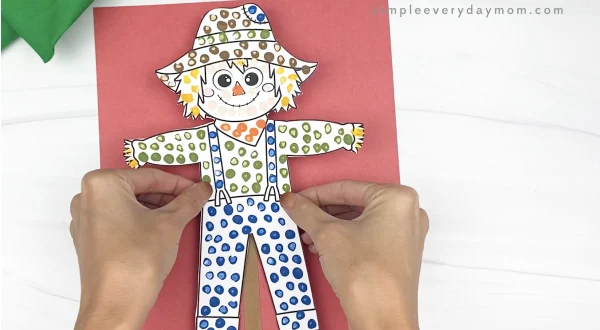 hand gluing paper scarecrow to red paper
