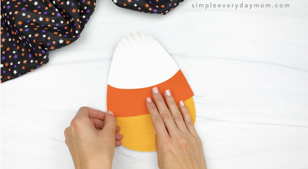 hand gluing orange paper onto paper plate candy corn craft