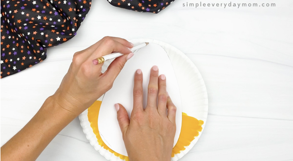 hand tracing candy corn template onto paper plate