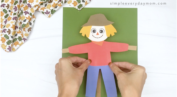 hand gluing paper scarecrow to green paper