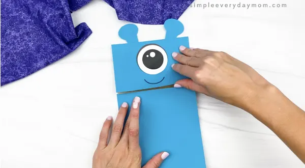 hand gluing body to alien paper bag puppet craft
