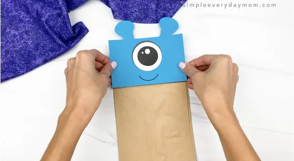 hand gluing head to alien paper bag puppet craft