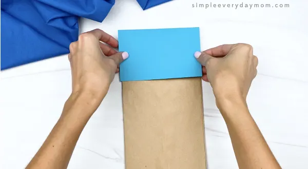 hand gluing blue rectangle to brown paper bag