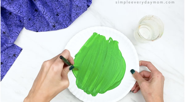 hands painting paper plate green