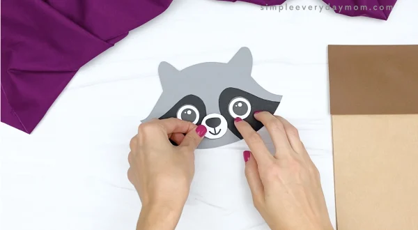 hand gluing nose and mouth to paper bag raccoon craft