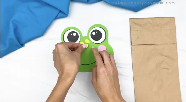 hand gluing spot to paper bag frog head