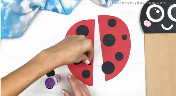 hand gluing spots to paper bag ladybug wings
