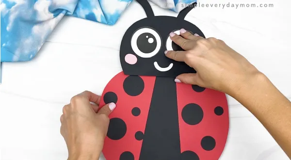 hand gluing body to ladybug paper bag craft