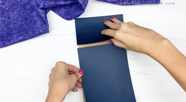 hand gluing dark blue paper to brown paper bag