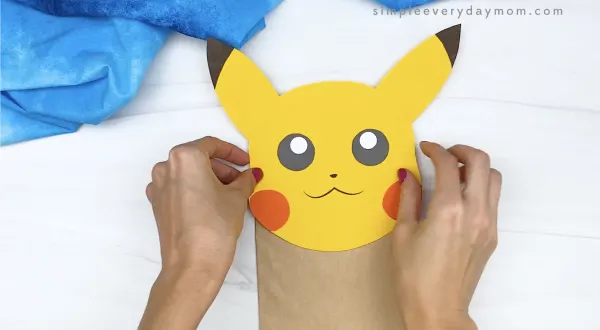 hand gluing head to paper bag Pikachu craft