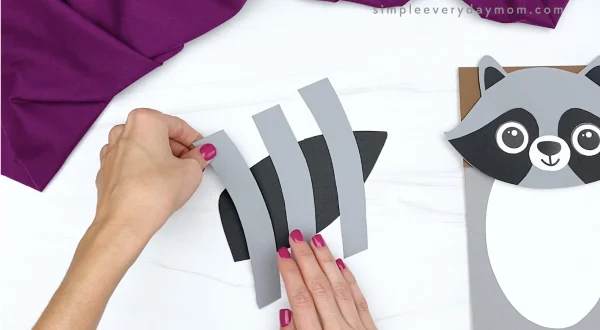 hand gluing stripes to tail of paper bag raccoon craft