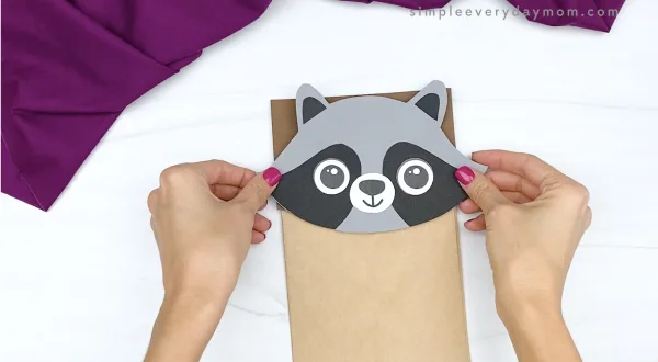 hand gluing head to paper bag raccoon craft
