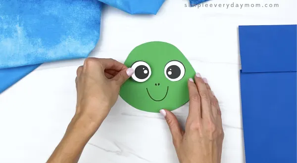 hand gluing eye to paper bag turtle head