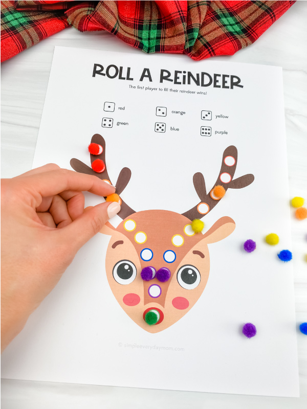 hand placing pom pom on printable roll a reindeer game