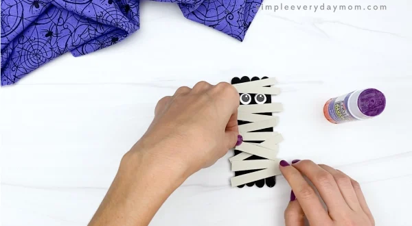 hand gluing wraps onto popsicle stick mummy craft