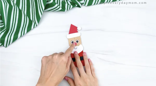 hand gluing pom pom nose to popsicle stick Santa craft