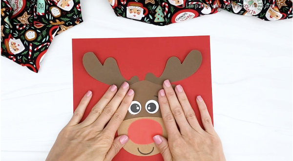 hand gluing reindeer head to red paper
