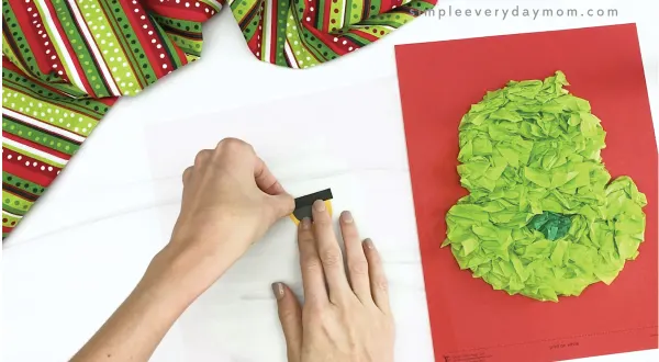 hand gluing eyebrow to eye of tissue paper grinch