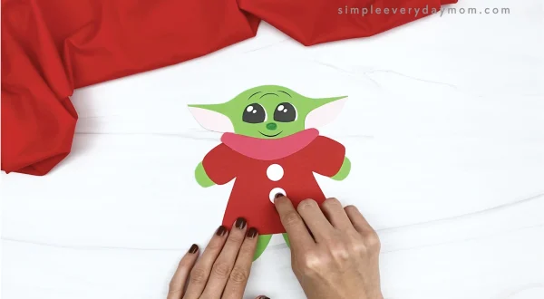 hand gluing buttons to baby Yoda gingerbread craft