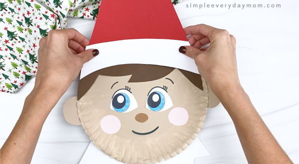 hands gluing hat onto paper plate elf on the shelf craft