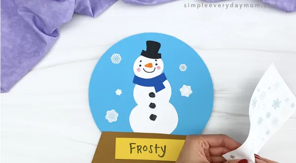 hand placing sticker snowflakes on snowman snowglobe craft