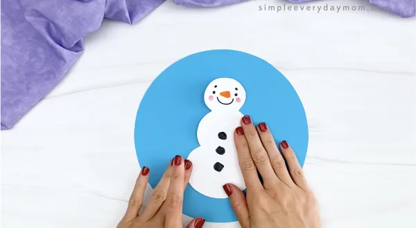 hand gluing snowman to blue circle