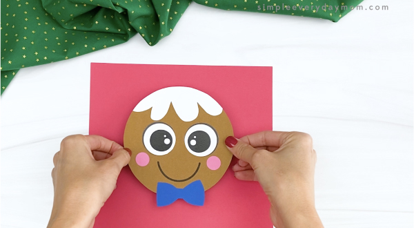 hands gluing gingerbread man head to red paper