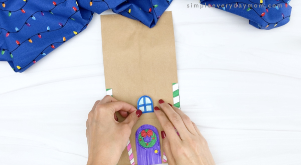 hand gluing window onto paper bag gingerbread house