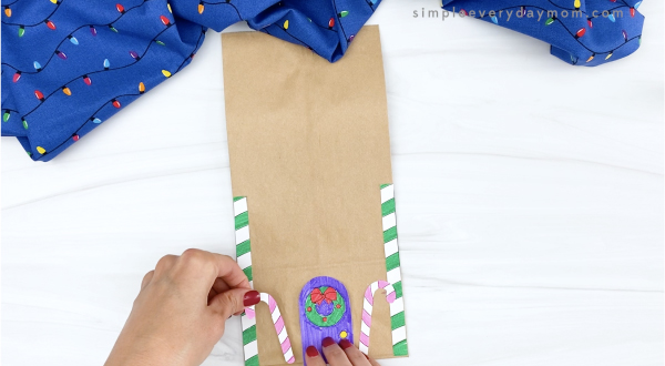 hand gluing candy cane onto paper bag gingerbread house
