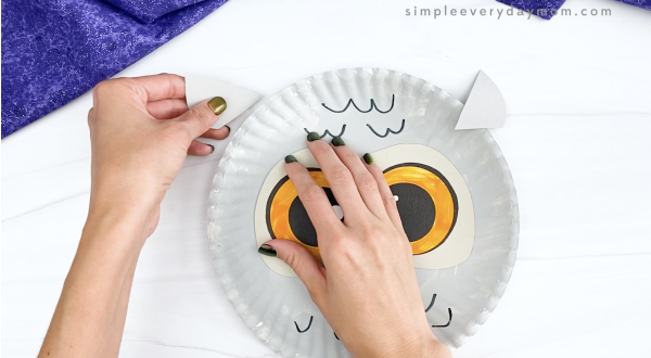 hand taping ears to paper plate snowy owl craft