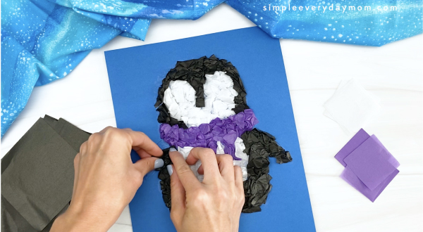 hand gluing tissue paper to penguin craft