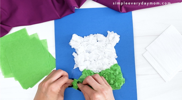 hand gluing green tissue paper to polar bear craft