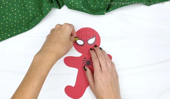 hand gluing eyes to spiderman gingerbread craft
