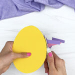 hands trimming excess paper off of paper Easter egg craft