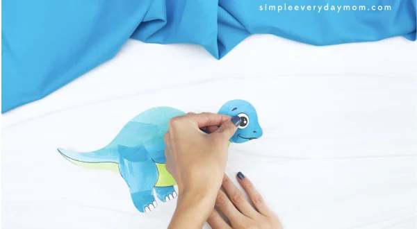 hand gluing eye to dinosaur cut and paste craft