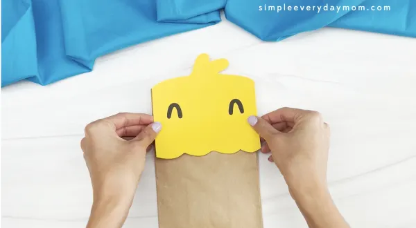 hands gluing head to chick paper bag puppet